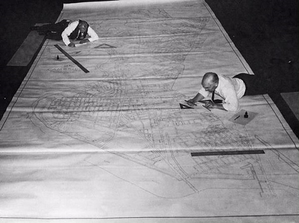 Black and white image showing two people working on a giant map