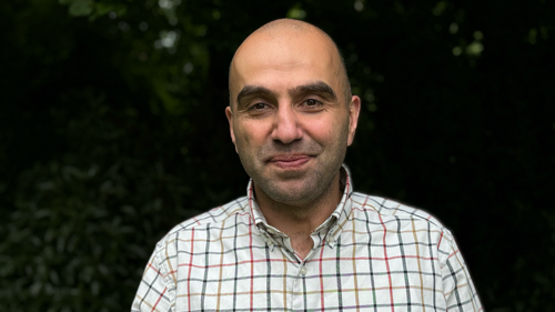 Colour photograph of Husam Al Waer wearing a collared cream shirt with red and blue checks