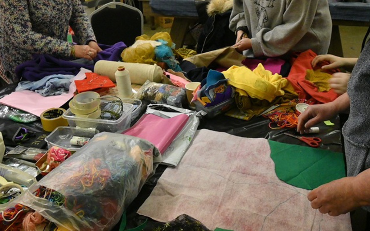 Three people at a table of art and craft materials making a colourful image.