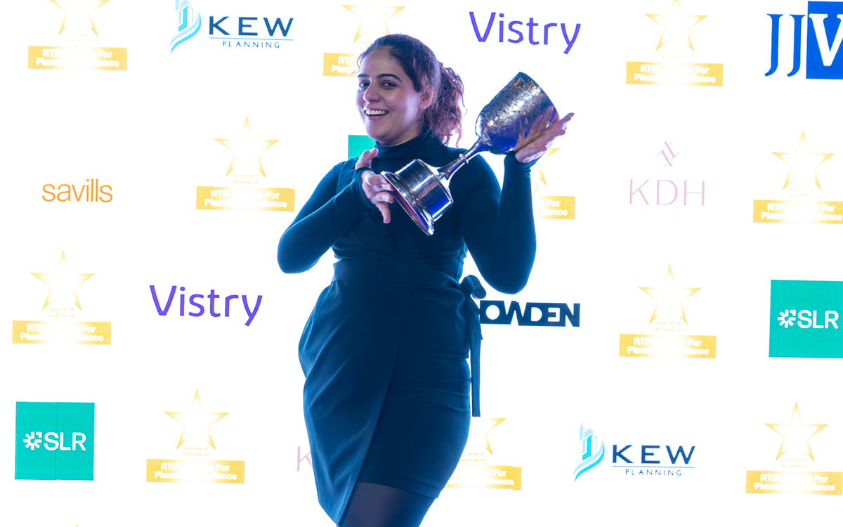Winner with trophy at the Awards for Planning Excellence 2025 ceremony with sponsor backdrop