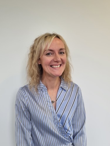 Colour image of Laura Robertson looking into the camera against a cream background light blue collared shirt with black and white diagonal stripes
