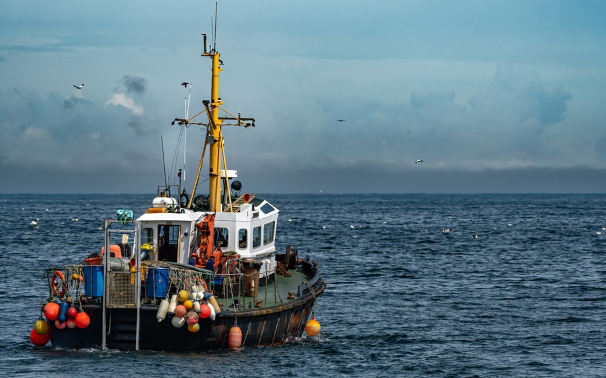 A small fishing boat with a yellow mass setting off towards a calm dark blue open sea with a lighter blue sky